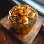 Cajun Pickled Shrimp: 1 Easy Recipe You’ll Love 7 Cajun Pickled Shrimp in a glass jar with lemon slices, chili flakes, and savory marinade on a wooden cutting board
